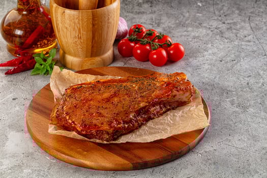 A piece of meat on a wooden plate with a knife and a bottle of vinegar photo