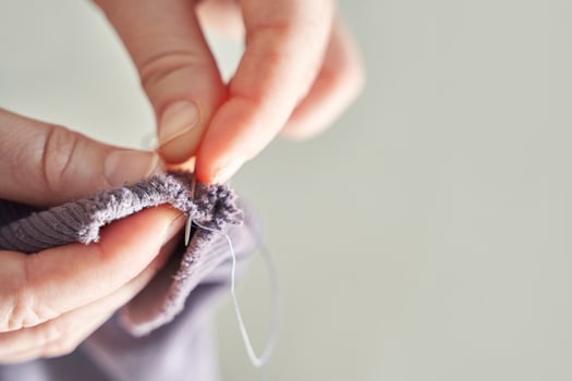 Close-up of adult hands sewing fabric with needle and thread for handcrafted clothing. photo