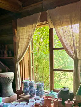Window in country house with curtains made of coarse burlap, clay products on windowsill. Potters workshop. photo