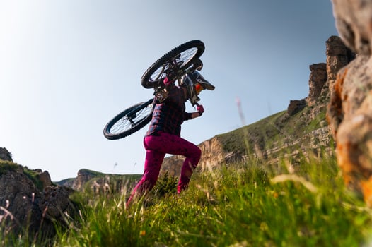 man in cycling gear walks along a trail carrying a mountain bike on his shoulder. A young man takes his bike and carries it up the mountains photo