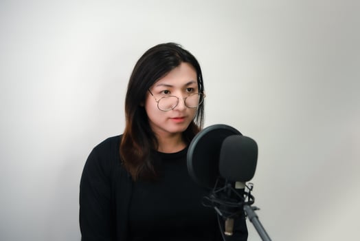 A woman in glasses is recording into a microphone photo