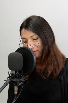 A woman wearing glasses and a black shirt is singing into a microphone photo