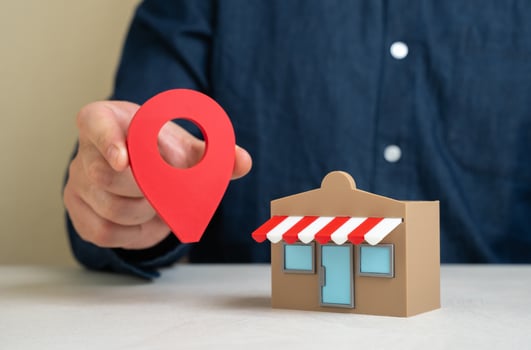 A man holds a geolocation pin near a store. Convenient location and high customer traffic. Business visibility. Role of location in boosting sales, branding, and competitive edge. photo