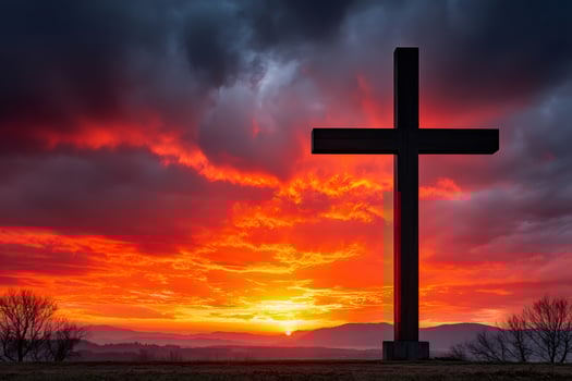Large christian cross standing on hilltop at sunset with dramatic red sky photo
