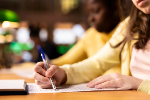 Multiethnic teens finishing their homework at a library after classes, engrossed in literature and notes. Pupils writing an essay for the school assignment, productive study sessions. Close up. photo