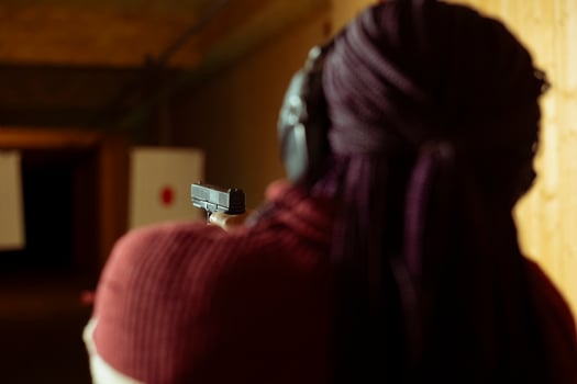 Woman in firing range doing shooting activity with pistol, wearing earmuffs to protect hearing. Person in shooting gallery training with firearm, using safety gear to prevent damage from gunshots photo