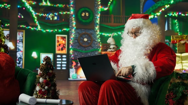 Man dressed as Santa Claus responding to kids requesting gifts, typing on laptop. Person impersonating Santa Claus asking children what they want for Christmas using notebook keyboard, camera A photo