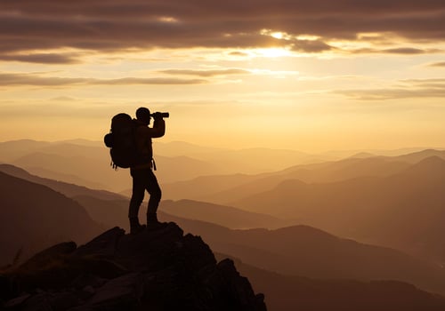 A man with a backpack standing on top of a mountain with a camera photo