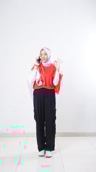 Indonesia independence day celebration with Asian girl wearing red and white Indonesia flag color attribute talking on the phone call and showing OK sign with hand gesture isolated on white background photo