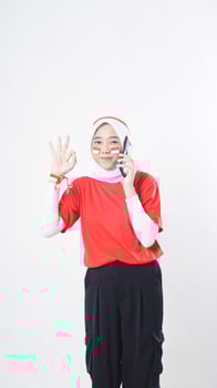 Indonesia independence day celebration with smiling Asian girl wearing red and white Indonesia flag color attribute talking on phone call while showing OK hand gesture isolated on white background photo