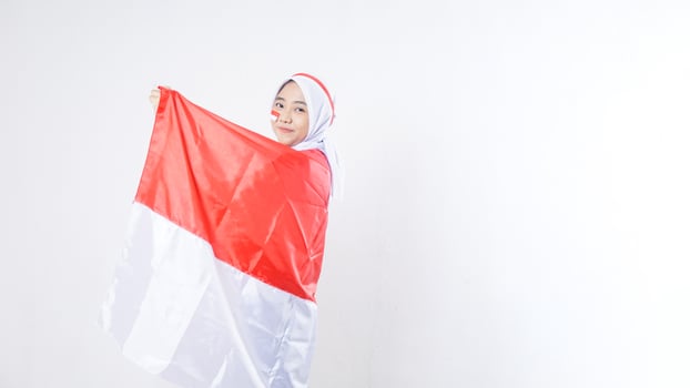 Beautiful Asian girl celebrate Indonesia independence day in red and white outfit holding and wrapping herself with Indonesian flag isolated on white background photo