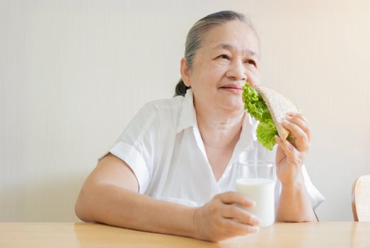 Happy portrait of senior Asian woman sitting on wooden table while eating vegetable sandwich and milk photo