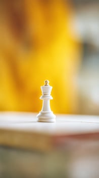 White Chess Queen on a Table Against a Yellow Background. A Close Up Image of a Single Chess Piece. photo