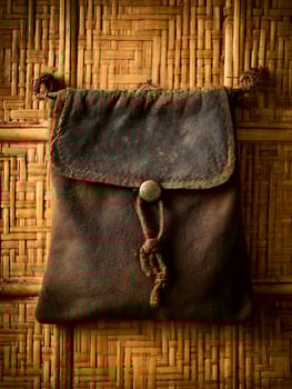 Antique Leather Pouch Hanging on Woven Bamboo Background. A close up image of a rustic, aged leather bag. photo