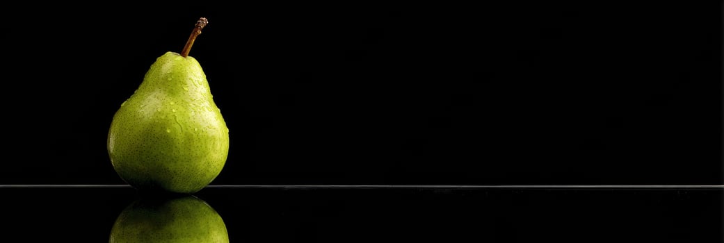 Single Green Pear on Reflective Black Surface Showcased With Dramatic Lighting and a Blank Top Margin Creating Visual Intrigue photo