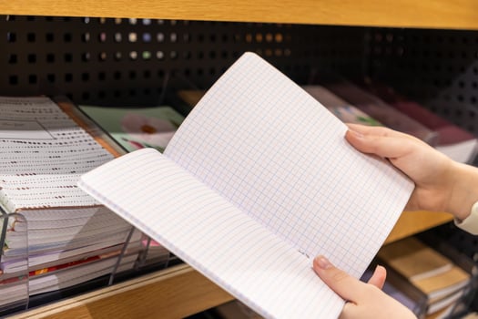 Person's hands carefully holding an open blank grid-lined notebook in a stationery store, ideal for students, office supplies, or creative planning photo