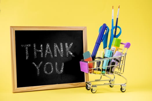 Thank You message on blackboard, next to a mini shopping cart filled with colorful school supplies, symbolizing appreciation for education or retail photo