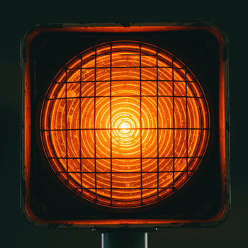 Close up of a bright orange traffic signal light with a protective grid against a dark background photo