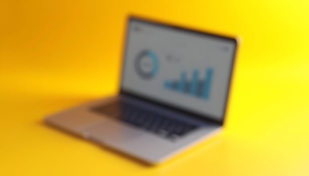 Blurred Laptop Displaying Business Charts on Yellow Background photo