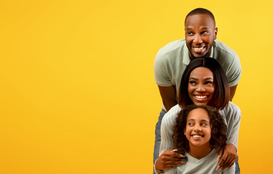 Positive african american family of three looking aside at empty space on yellow studio background, standing behind each other. Look there, promo and cool offer concept. Free space for advertisement photo