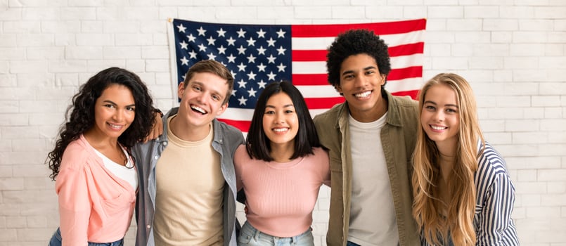 Fun education, language courses, learn english and exchange students. Young smiling people of different nationalities hug in college with large USA flag on white brick wall, free space, studio shot photo