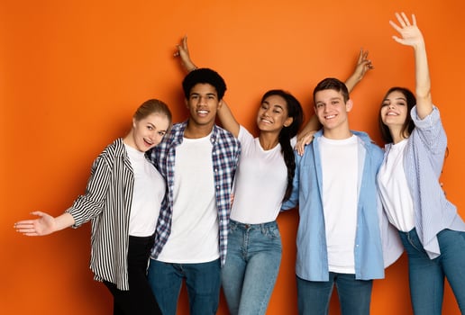 Positive teen friends embracing and rejoicing holidays, posing to camera over orange wall photo