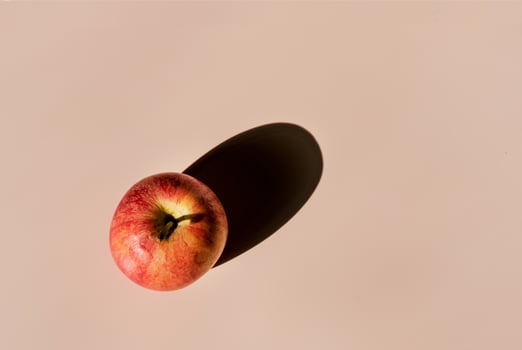 one red apple on beige background, with hard shadow, copy space photo