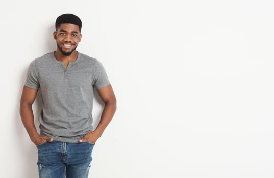 Young african-american casual man with his hands in his pockets, smiling to camera, white studio background with copy space photo