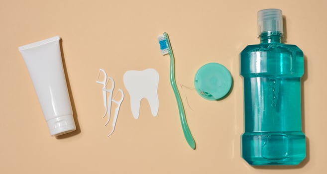 Oral hygiene set including a tube of toothpaste, a toothbrush, dental floss and a bottle of mouthwash, beige background. Top view. photo