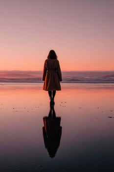 A woman in a coat stands on the beach at sunset photo