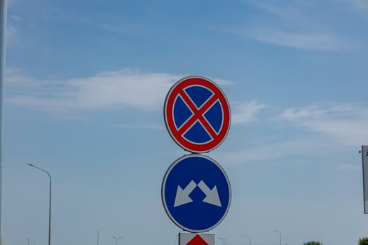 Two road signs indicating no parking and a specific direction are prominently placed against a bright blue sky, highlighting traffic regulations photo