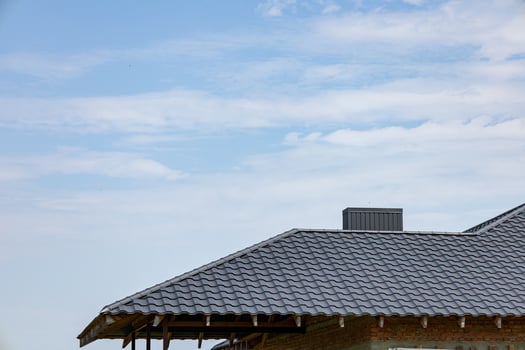 Construction workers are installing new metallic tiles on the rooftops of a building while the sky features soft, scattered clouds photo