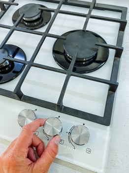 A person is slowly and deliberately turning the knob on a gas stove, which is a kitchen appliance specifically designed for the purpose of cooking a wide variety of food and meals photo