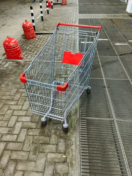 On a bright and sunny day, a shopping cart featuring a striking red handle is parked neatly on the sidewalk, patiently waiting to be picked up and used by nearby potential shoppers photo