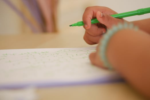 Child practicing writing with a green marker at home photo