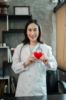 Female doctor in white coat holding a red heart, symbolizing health and care, in a modern medical office. photo