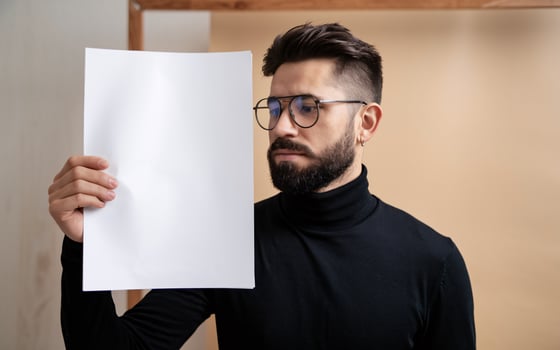 A man with glasses holding up a blank sheet of paper photo