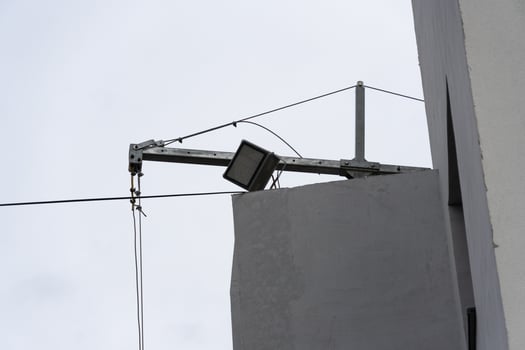 Overhead light fixture is mounted on a cable stretching across a building, reflecting an urban setting in broad daylight photo