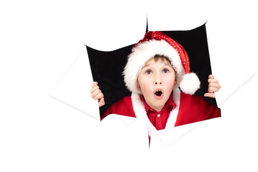 Child Santa Claus looks out of a hole in paper. The boy at Christmas is surprised. photo