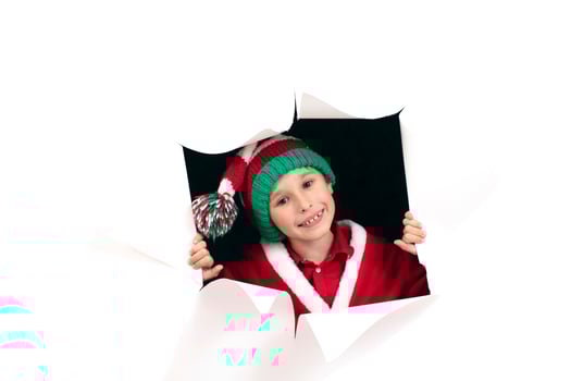 Child Santa Claus looks out of a hole in paper. A boy in a New Year's costume is smiling. Holiday surprise. Christmas holiday concept photo
