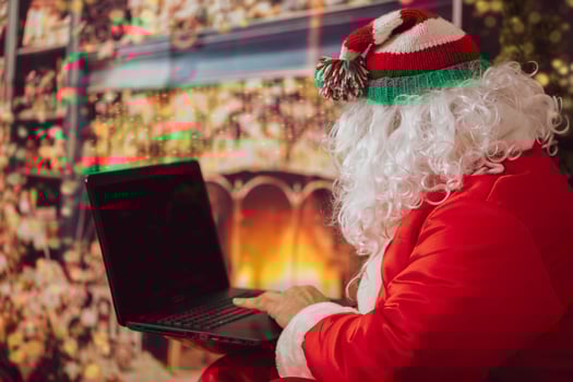 Santa Claus is looking at the laptop. A man in a Christmas suit at the computer on the background of New Year's lights. The modern wizard. Christmas holidays concept photo