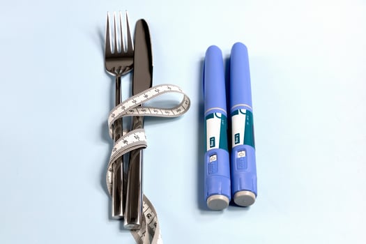 Concept of losing weight with Ozempic. Knife, fork wrapped in a measuring tape and two syringes nearby photo