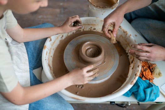 Boy shaping wet clay into a jug in warm light of a craft pottery class photo