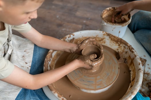 Child and instructor shaping wet clay together at pottery wheel during a hands-on ceramic workshop photo