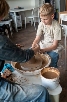 Boy and female instructor shaping clay together at pottery wheel, kids learning traditional craf photo