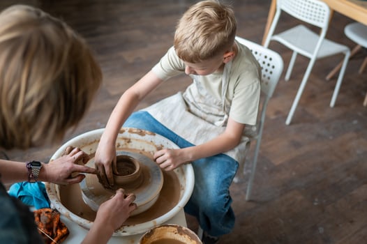 Boy and female instructor shaping clay together at pottery wheel, kids learning traditional craft photo