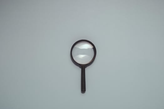 Classic magnifying glass with black handle and clear lens, centered vertically on smooth, muted blue. Ideal for search, investigation, discovery, research, and analysis. photo