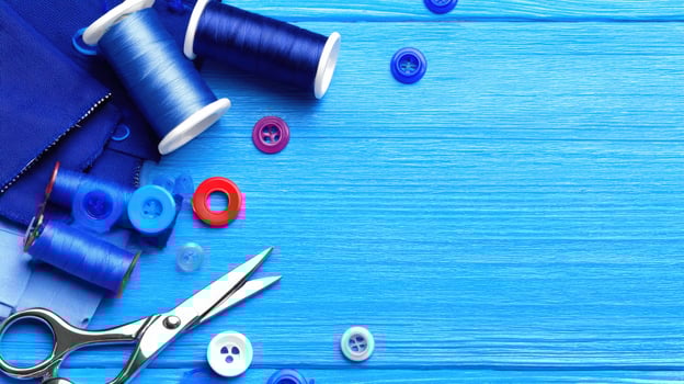 Blue fabric, sewing thread, scissors and sewing needles on a wooden table photo