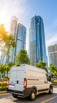 A white van is driving down the road in front of tall buildings photo