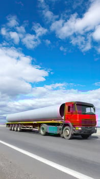 A large truck driving down the road with a large pipe on the back photo